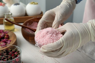 Photo of Woman in gloves making bath bomb at white table, closeup