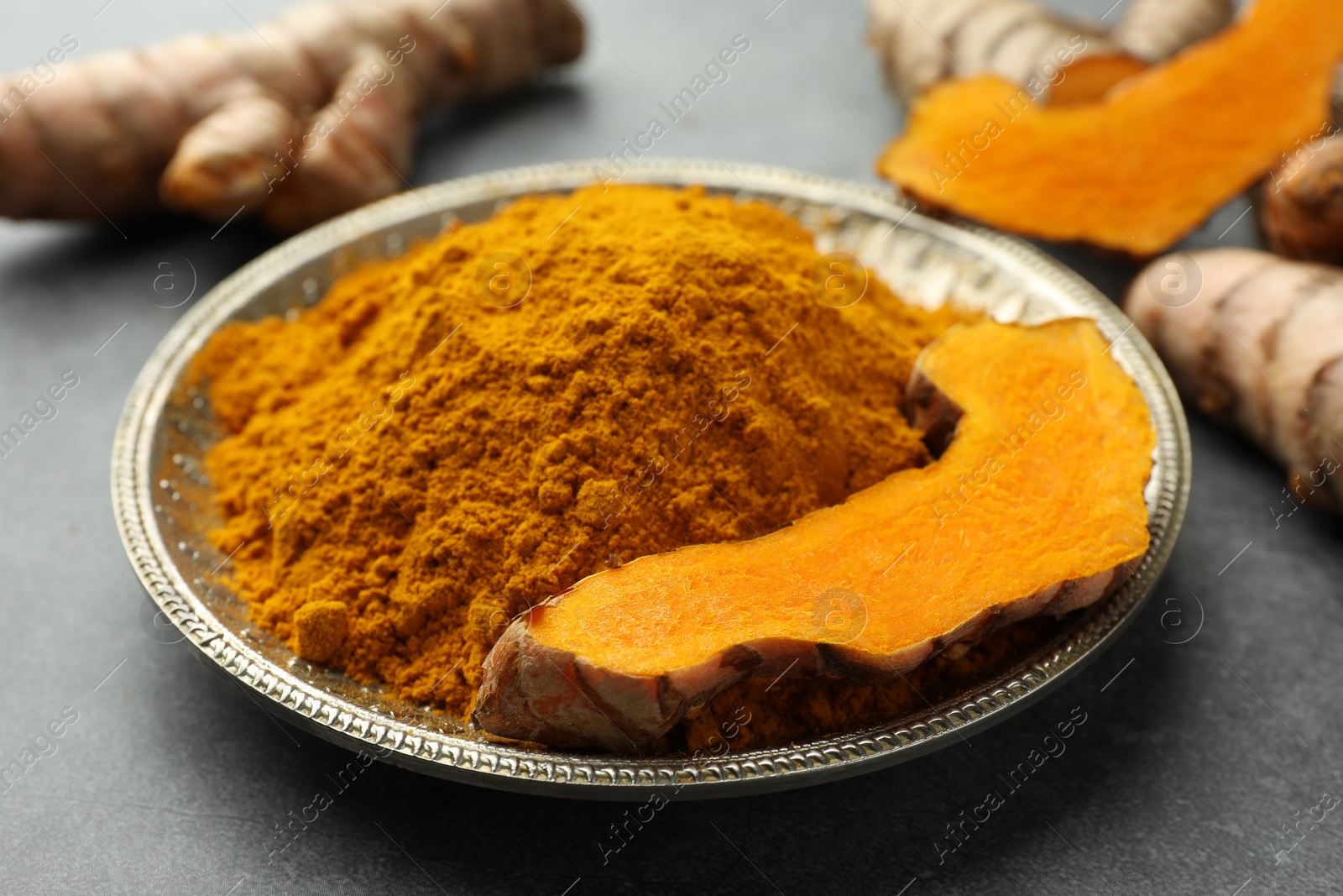 Photo of Plate with turmeric powder and cut root on grey table, closeup