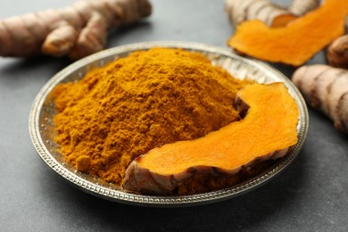 Photo of Plate with turmeric powder and cut root on grey table, closeup