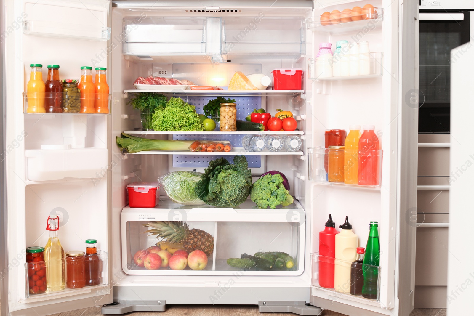 Photo of Open refrigerator filled with different food in kitchen