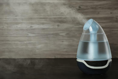 Photo of Modern air humidifier on wooden table. Space for text