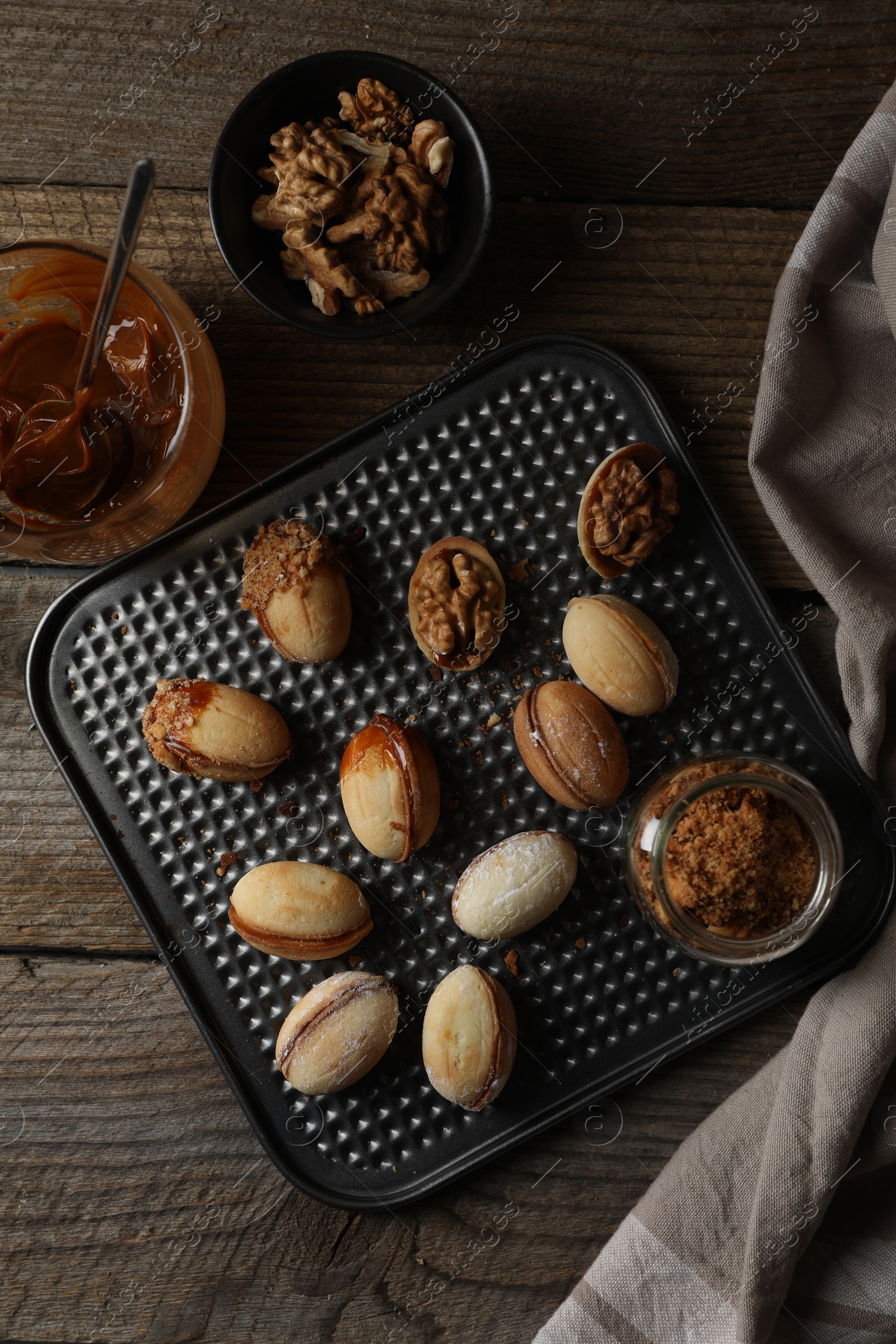 Photo of Freshly baked homemade walnut shaped cookies, boiled condensed milk and nuts on wooden table, flat lay