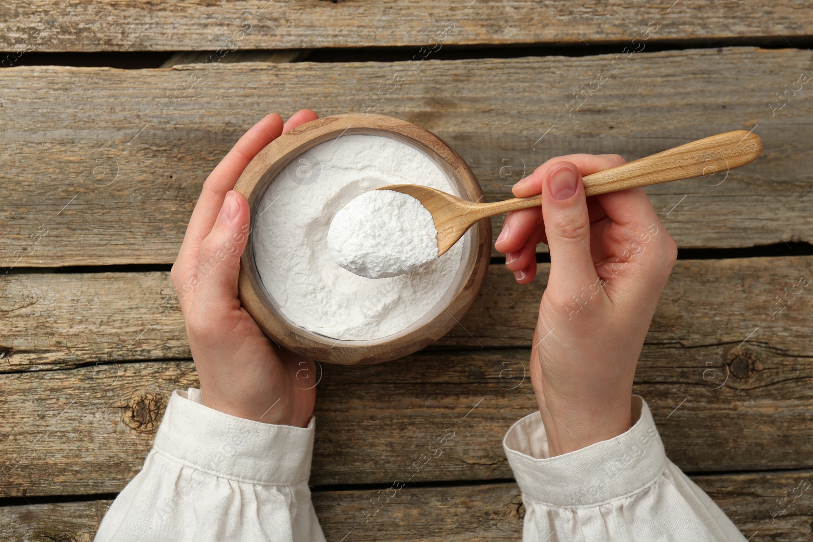 Photo of Woman taking baking powder with spoon from bowl at wooden table, top view