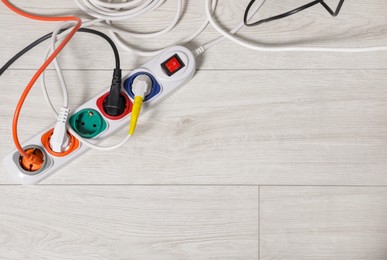 Photo of Extension cord with electrical plugs on white floor, flat lay. Space for text