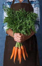 Photo of Woman holding ripe carrots on blue background, closeup