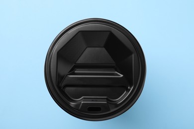 Photo of One paper cup with black lid on light blue background, top view. Coffee to go