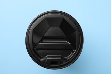 One paper cup with black lid on light blue background, top view. Coffee to go