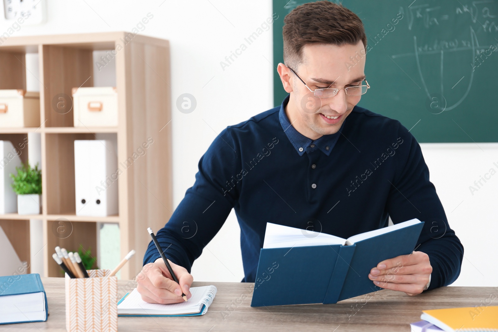 Photo of Young male teacher working at table in classroom