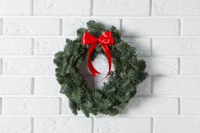 Photo of Christmas wreath made of fir tree branches with red ribbon on white brick wall