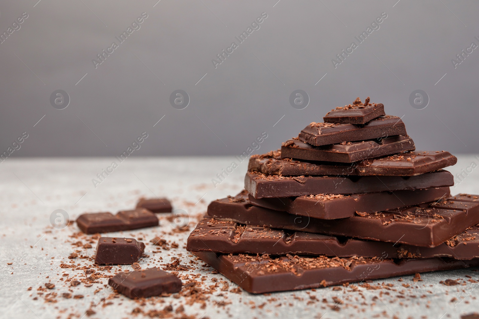 Photo of Pieces and shavings of tasty chocolate on light grey table, space for text