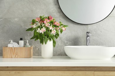 Photo of Vase with beautiful Alstroemeria flowers and toiletries near sink in bathroom