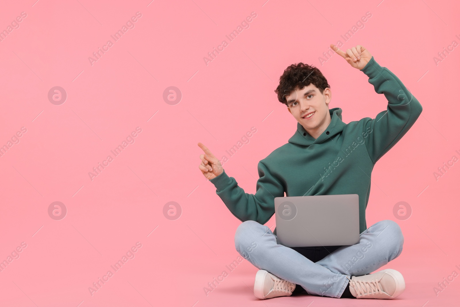 Photo of Portrait of student with laptop pointing on pink background. Space for text