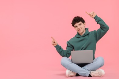 Portrait of student with laptop pointing on pink background. Space for text