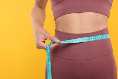 Photo of Slim woman measuring waist with tape on yellow background, closeup. Weight loss