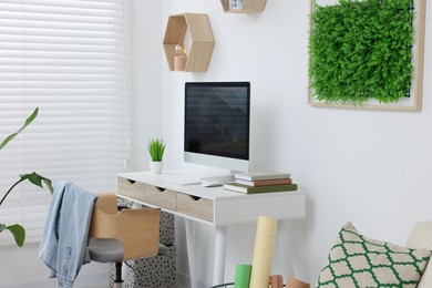 Green artificial plant wall panel and desk with computer in light room. Interior design