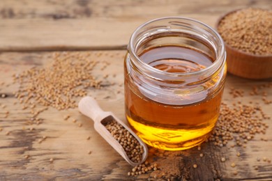 Photo of Jar of natural oil and mustard seeds on wooden table. Space for text