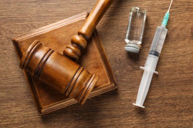 Photo of Law concept. Gavel, syringe and glass vial on wooden table, top view