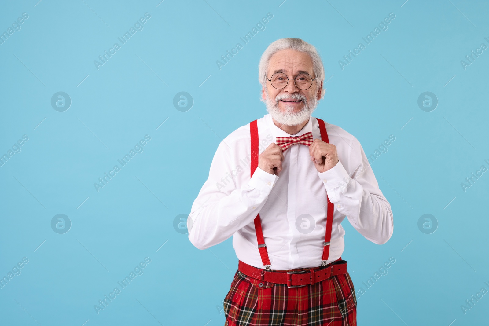 Photo of Portrait of stylish grandpa with glasses and bowtie on light blue background, space for text