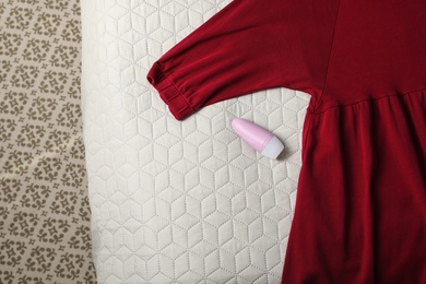 Photo of Female roll-on deodorant and clothes on bed, top view. Space for text