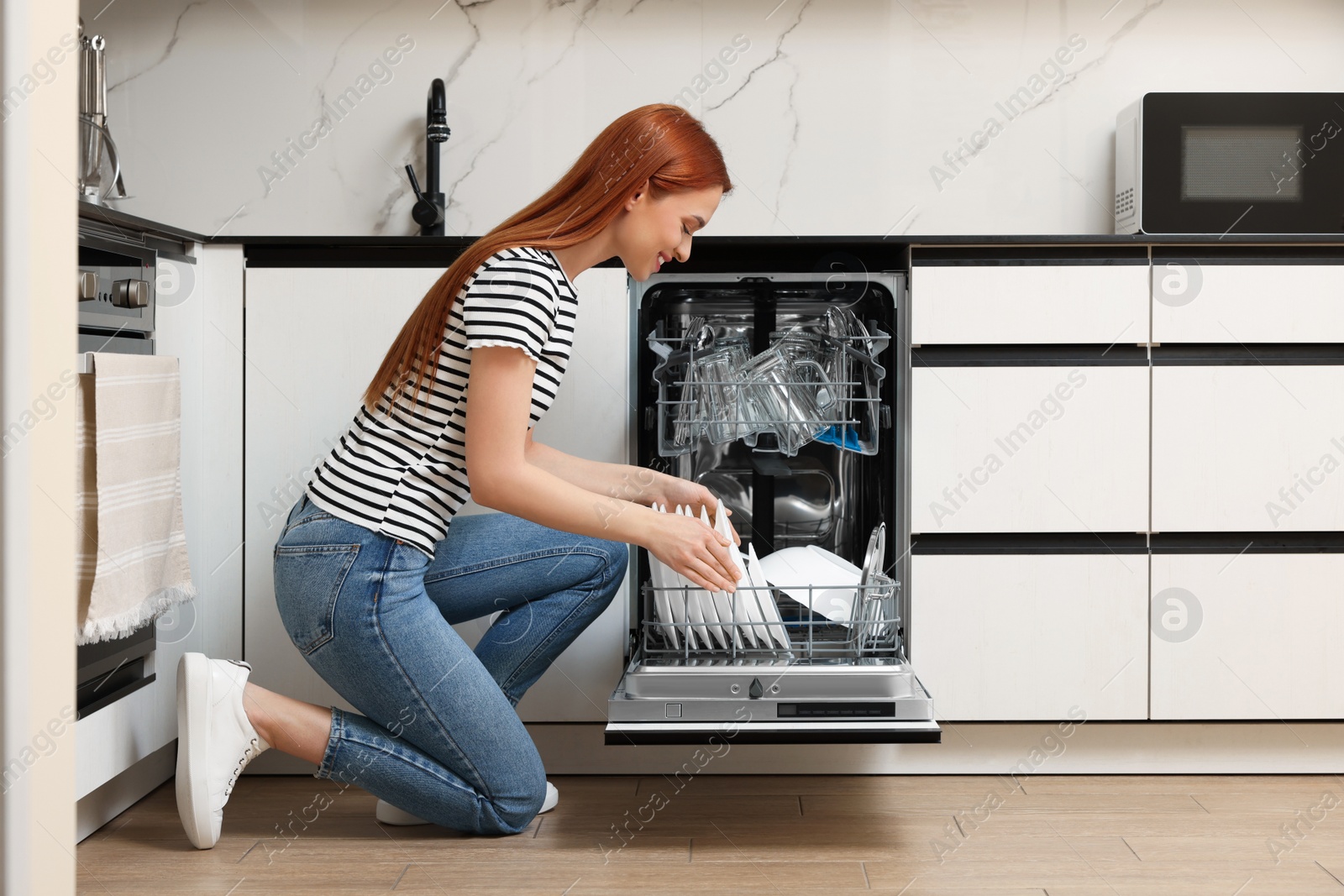 Photo of Smiling woman loading dishwasher with plates in kitchen