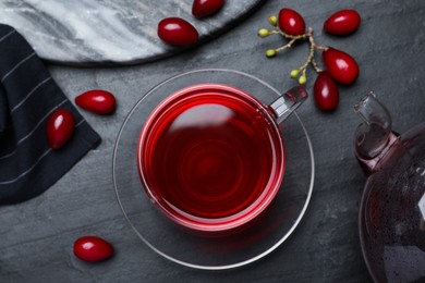 Photo of Glass cup of fresh dogwood tea and berries on black table, flat lay