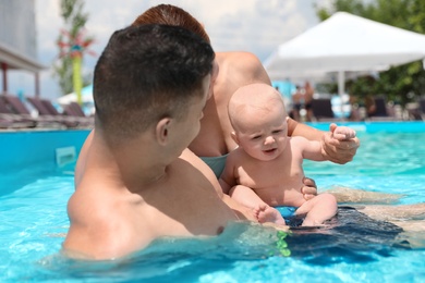 Happy parents with little baby in swimming pool on sunny day, outdoors