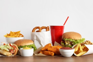 Photo of French fries, burgers and other fast food on wooden table against white background