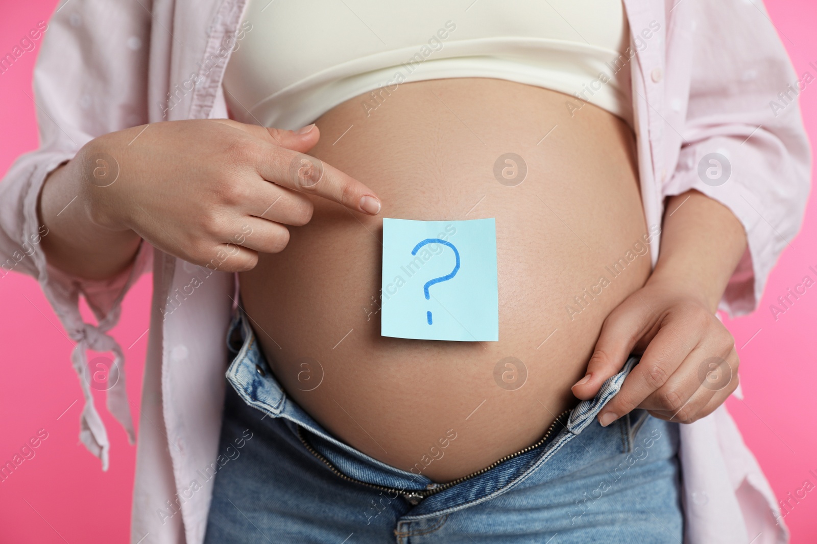 Photo of Pregnant woman with sticky note on belly against pink background, closeup. Choosing baby name