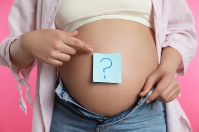 Photo of Pregnant woman with sticky note on belly against pink background, closeup. Choosing baby name