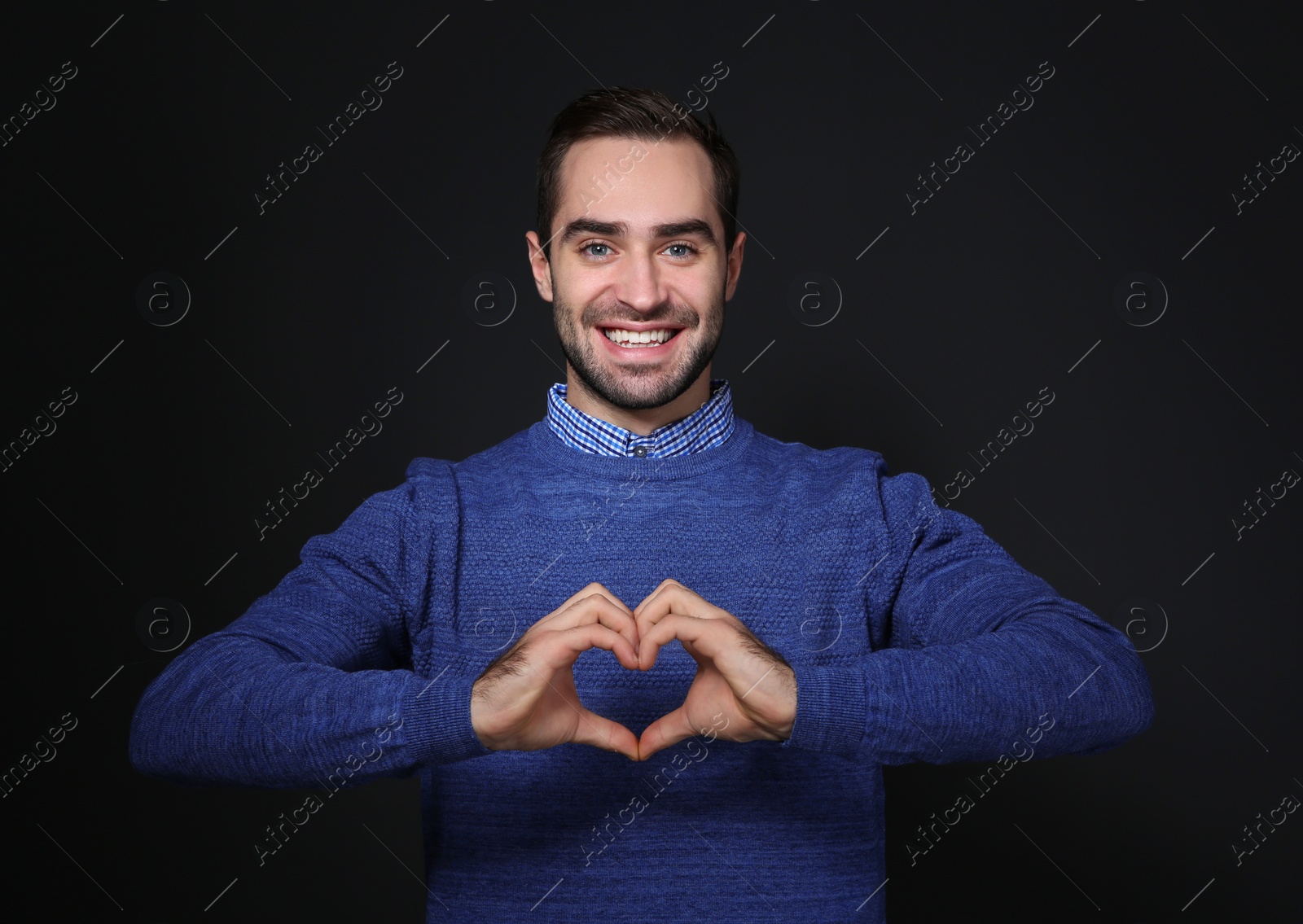 Photo of Man showing HEART gesture in sign language on black background