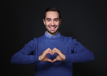 Photo of Man showing HEART gesture in sign language on black background