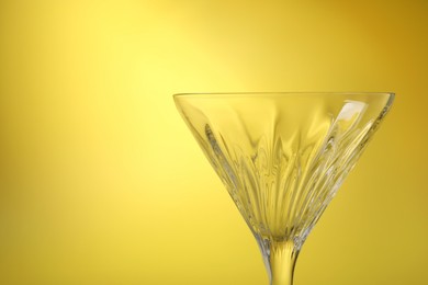 Elegant empty martini glass on yellow background, closeup. Space for text