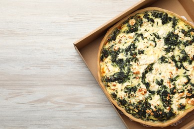 Delicious homemade spinach quiche in carton box on wooden table, top view. Space for text