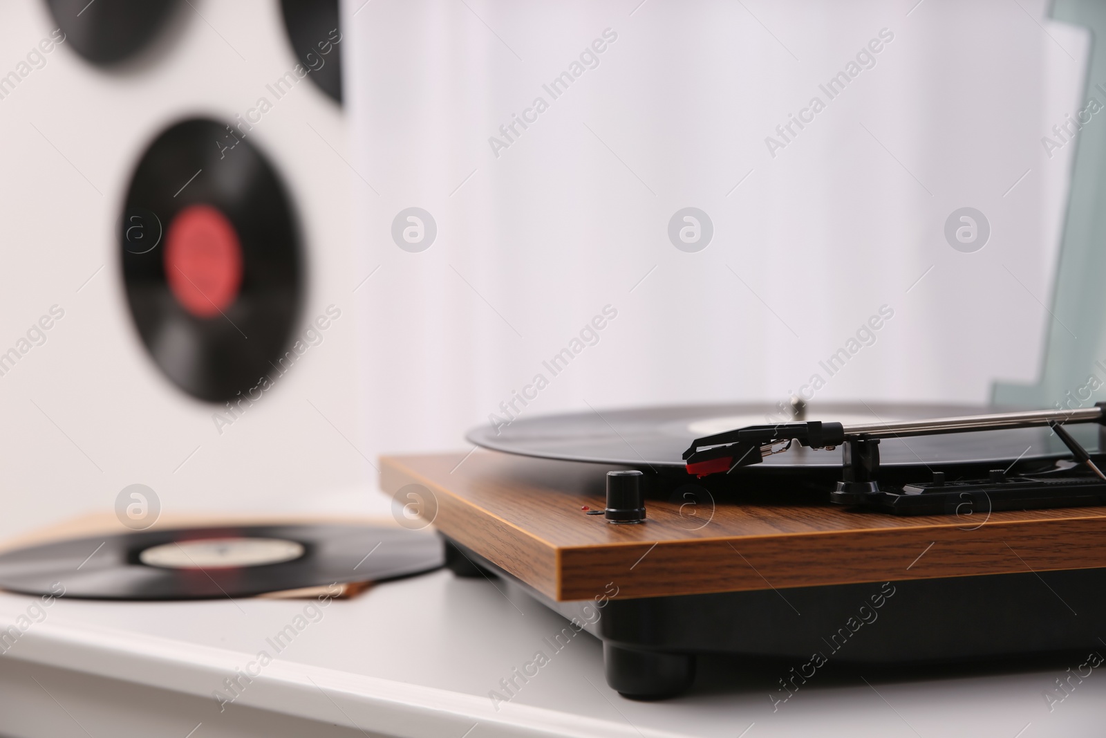 Photo of Stylish turntable with vinyl record on white chest of drawers indoors, closeup. Space for text