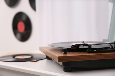 Stylish turntable with vinyl record on white chest of drawers indoors, closeup. Space for text