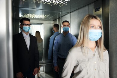 Photo of Group of people with face masks in elevator. Protective measure