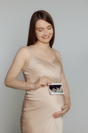 Pregnant woman with ultrasound picture of baby on light grey background