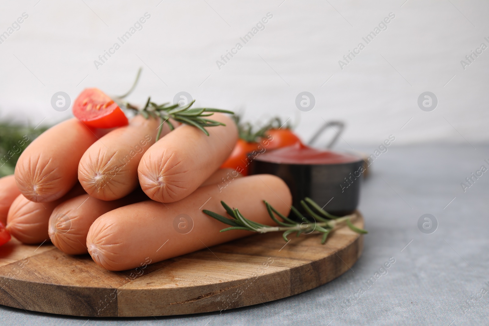 Photo of Delicious boiled sausages, tomato and rosemary on gray table, closeup