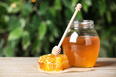 Photo of Tasty honey on table against green blurred background