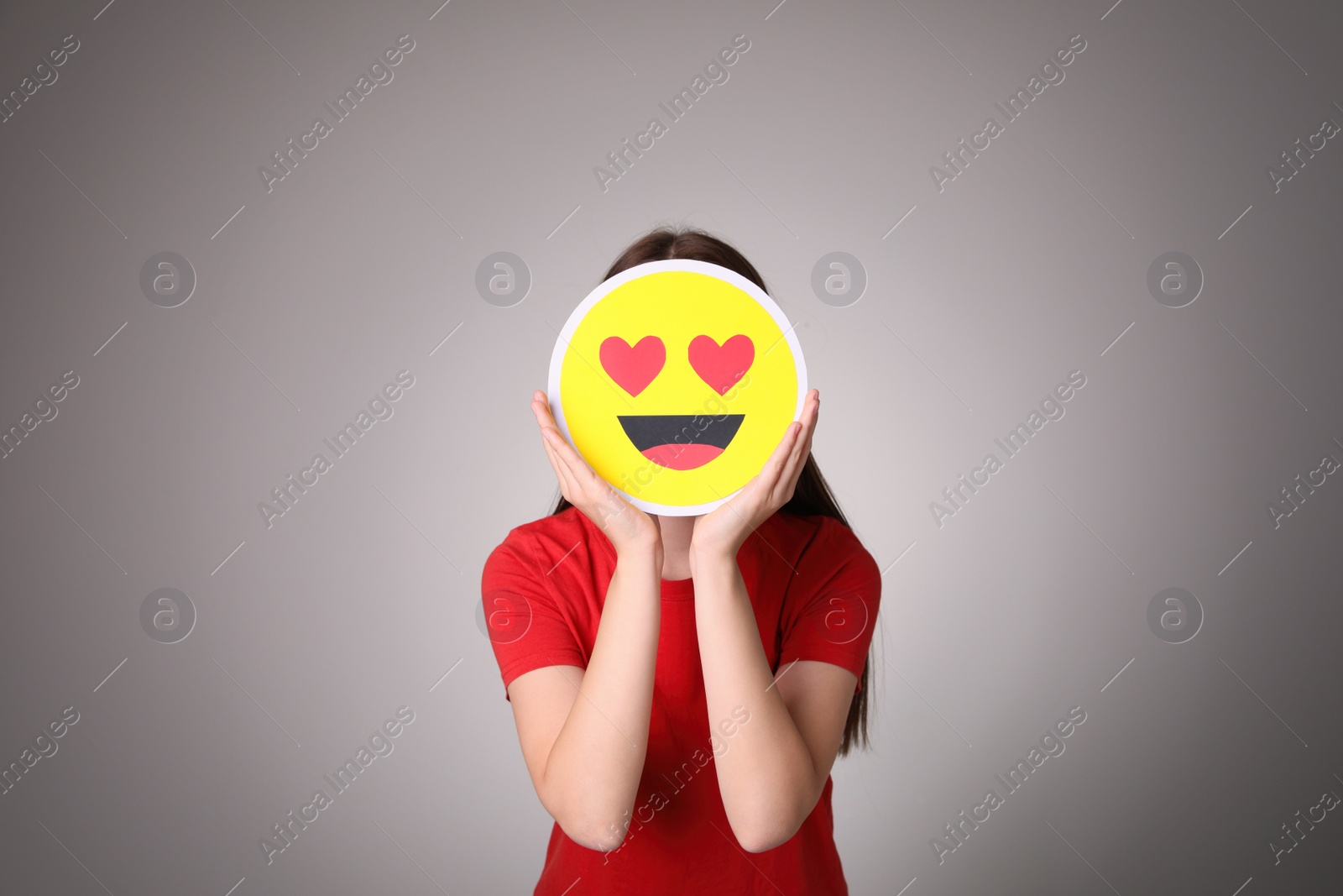 Photo of Woman covering face with heart eyes emoji on grey background