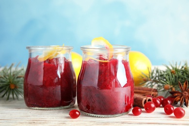 Photo of Tasty cranberry sauce with citrus zest in glass jars on table