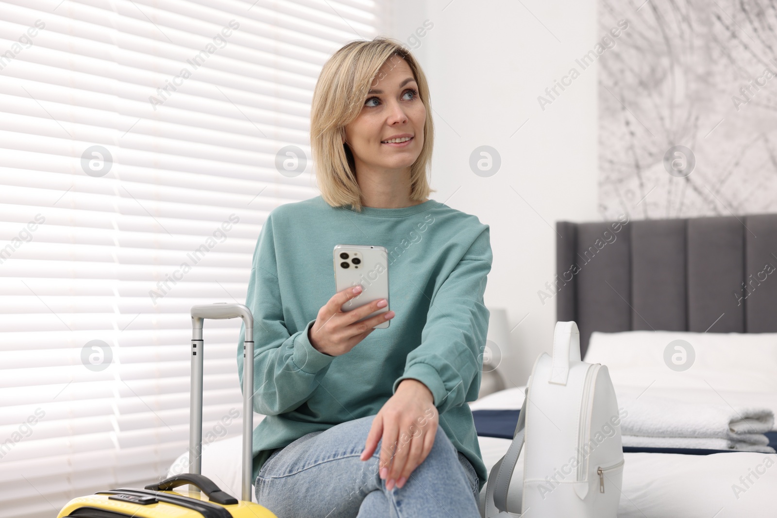 Photo of Smiling guest with smartphone in stylish hotel room