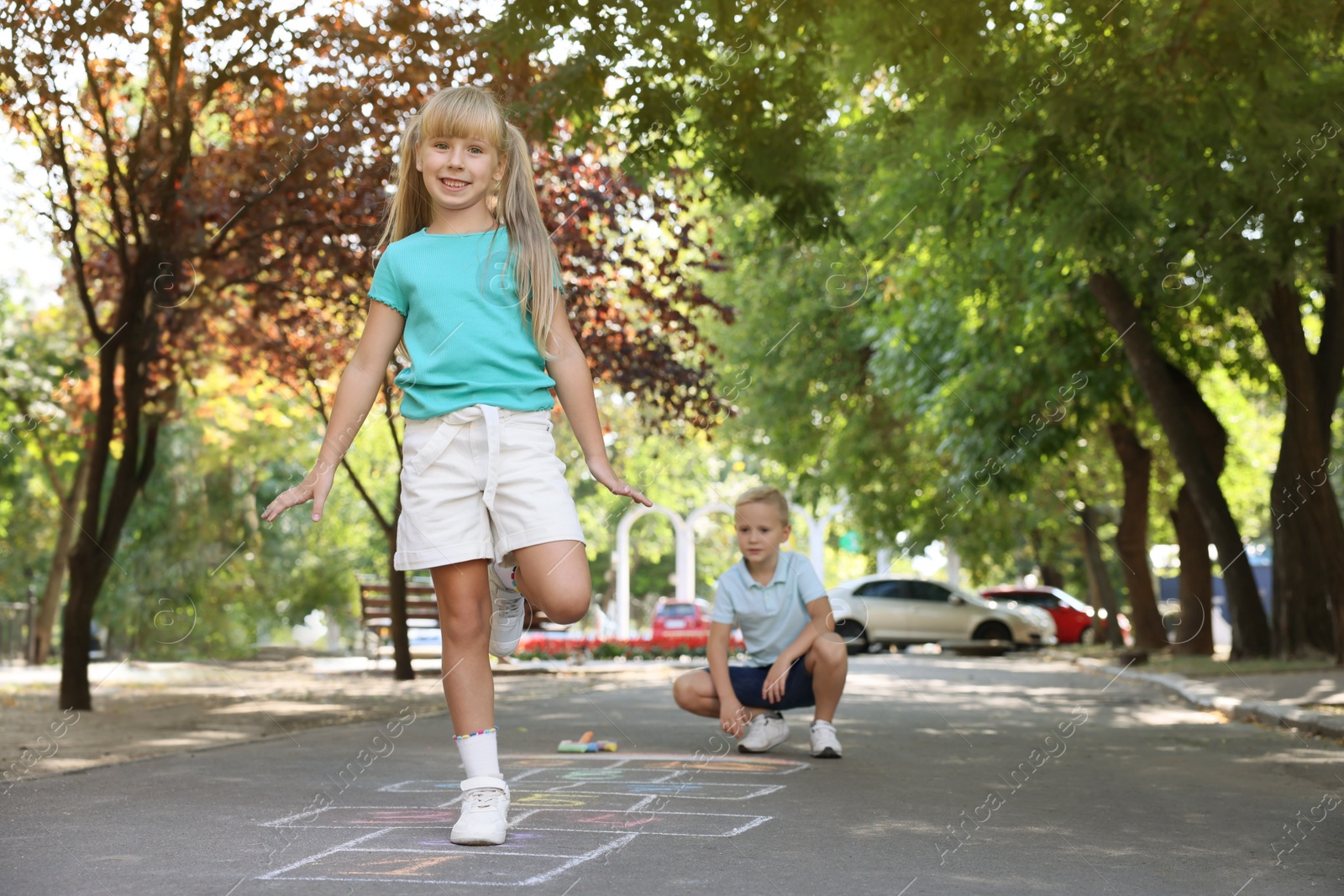 Photo of Little children playing hopscotch drawn with chalk on asphalt outdoors