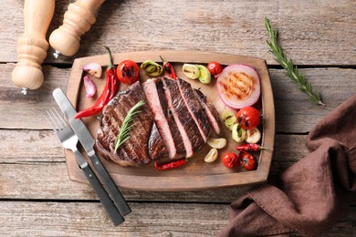 Photo of Delicious fried beef meat served with vegetables on wooden table, flat lay