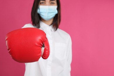 Woman with protective mask and boxing gloves on pink background, space for text. Strong immunity concept