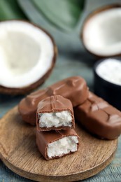 Photo of Delicious milk chocolate candy bars with coconut filling on blue wooden table, closeup. Space for text
