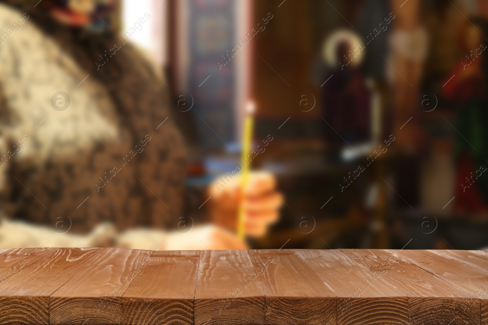 Image of Empty wooden table and blurred view of woman holding candle in church, space for text