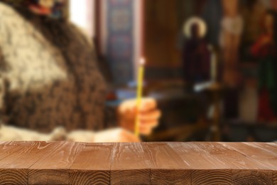 Image of Empty wooden table and blurred view of woman holding candle in church, space for text