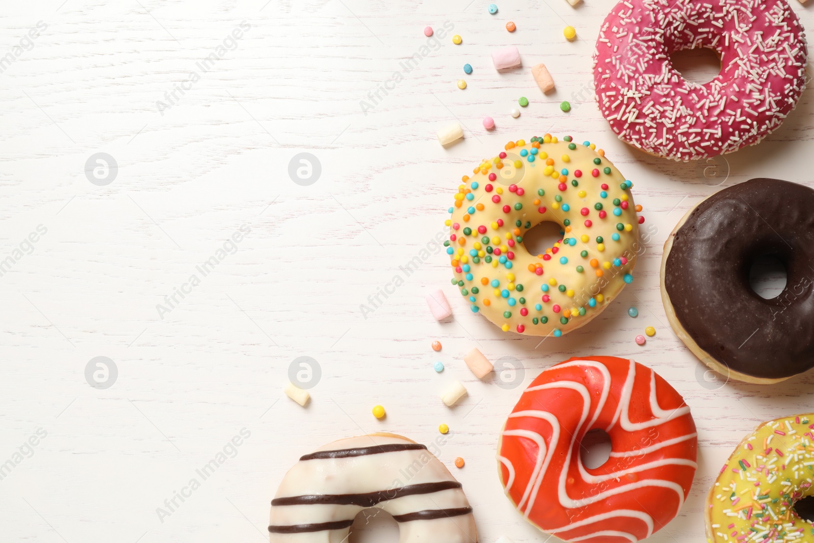 Photo of Delicious glazed donuts on white wooden table, flat lay. Space for text