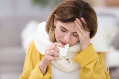 Photo of Sad woman with tissue suffering from cold on blurred background
